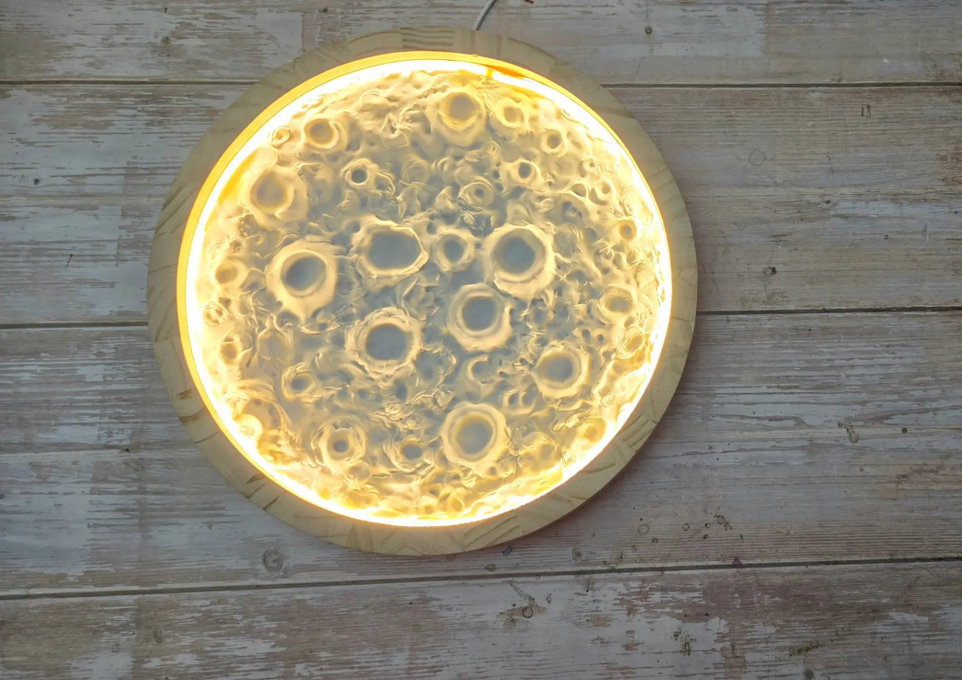 A glowing moon lamp with detailed crater texture on a rustic wooden table