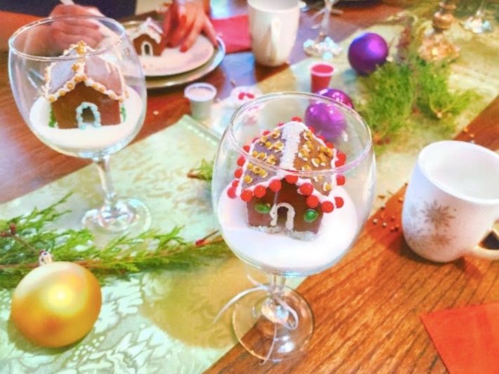 Mini gingerbread houses crafted inside wine glasses on a festive table
